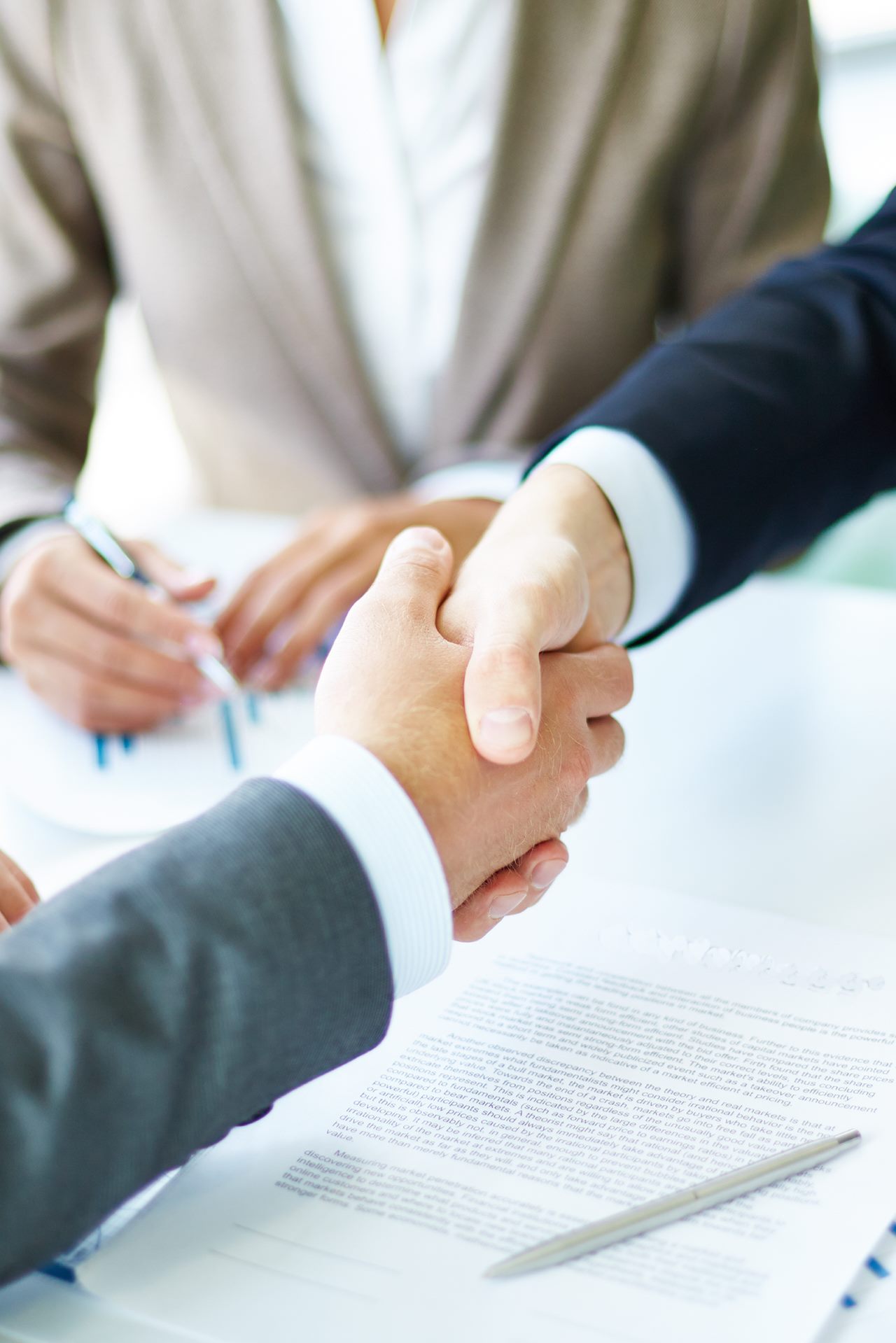 Image of business partners handshaking over business objects on workplace
